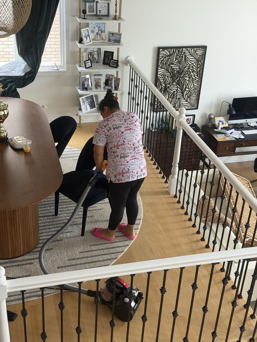 Jenny vacuuming a rug near a staircase in an open-concept home
